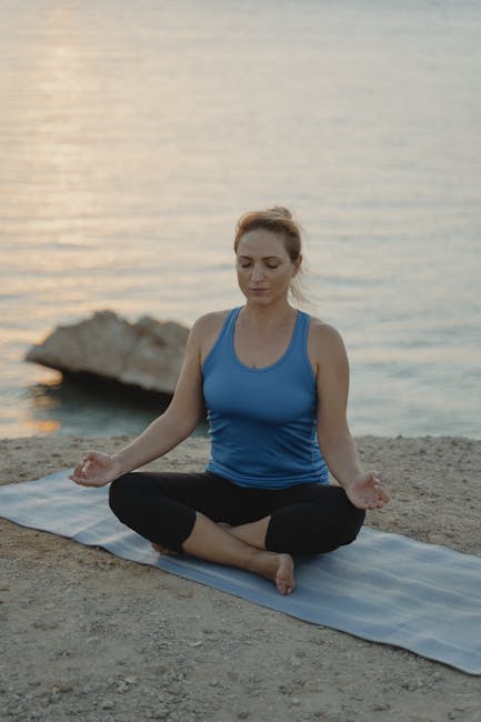 Woman peacefully doing a seated yoga pose in a warmly lit studio with her eyes closed.